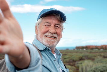 Portrait of happy senior bearded man outdoors in trekking day looking at camera. Elderly grandfather smiling enjoying healthy lifestyle and nature.