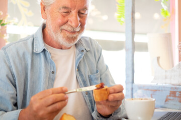 Adult senior man in coffee shop having breakfast with cappuccino and sweet food. Smiling elderly people enjoying retirement and free lifestyle