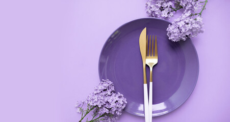 beautiful layout with lilacs, a plate and cutlery on a purple background. place for text. spring food concept for restaurant or cafe.