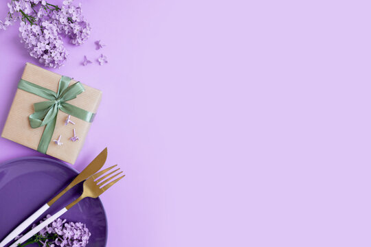 beautiful layout with lilacs, a plate and cutlery, a gift on a purple background. place for text. spring food concept for restaurant or cafe.