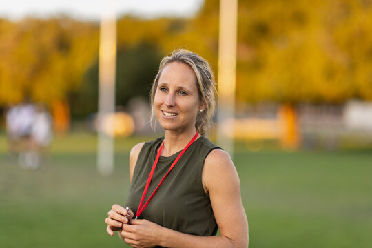 fit woman in her thirties on playing field with whistle