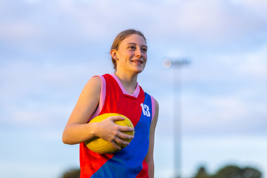 Teenage Girl In Football Uniform Carrying Aussie Rules Football Onto The Field