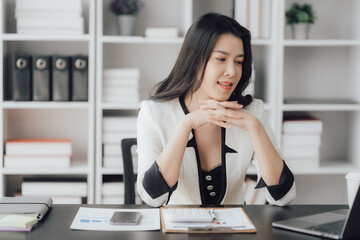 Cheerful business lady working on laptop in office, Asian happy beautiful businesswoman in formal suit work in workplace. Attractive female employee office worker smile.