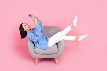 Full size portrait of pretty girl sit chair hold use smart phone chatting isolated on pink color...