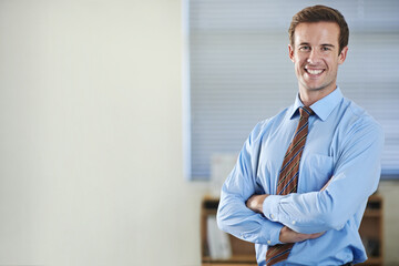 Fototapeta premium Climbing the corporate ladder. A young businessman standing and smiling with his arms folded - copyspace.
