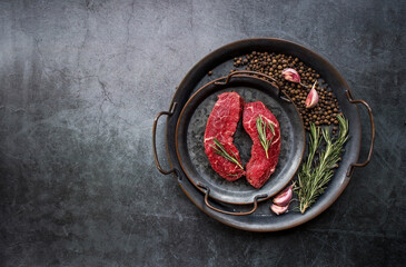 Fresh meat. Raw beef steaks with rosemary and spices on a stylish iron tray. Flat top view.
