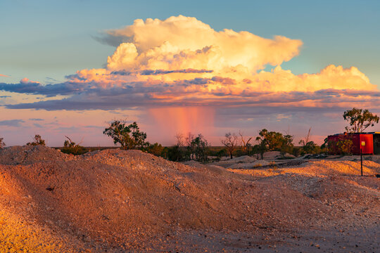 Rain falling from a large thunderstorm over an outback mining landscape at sunset