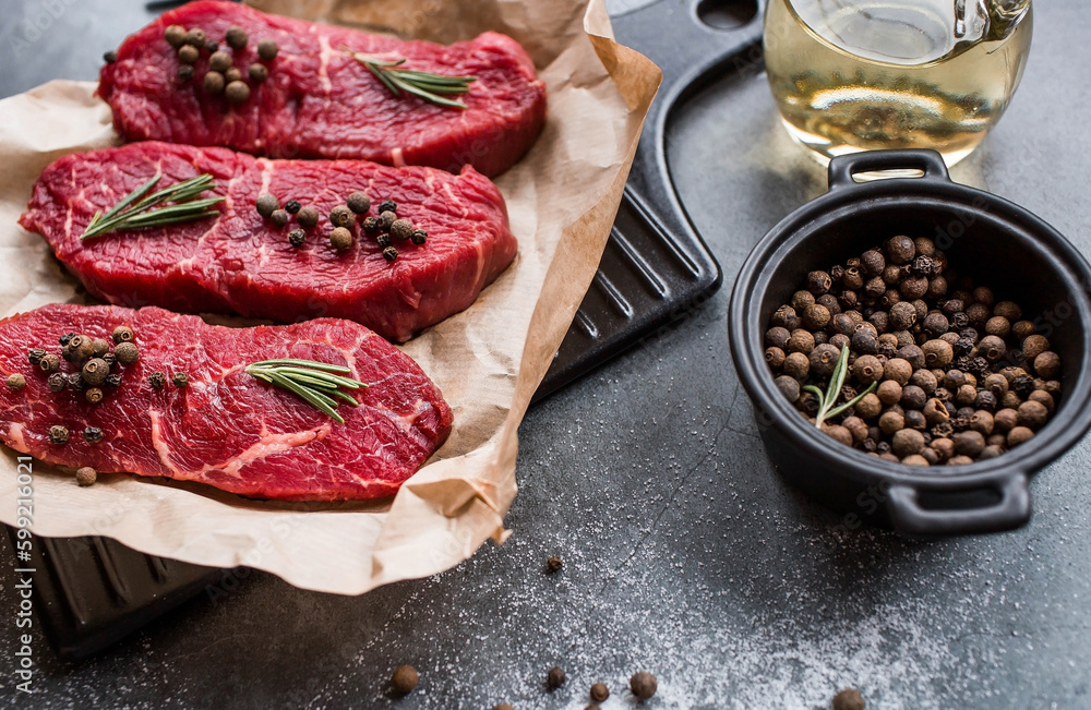 Wall mural fresh meat. raw beef steaks with rosemary and spices on parchment paper on a stylish board. flat top