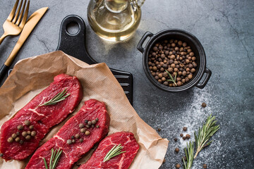 Fresh meat. Raw beef steaks with rosemary and spices on parchment paper on a stylish board. Flat top view.