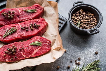 Fresh meat. Raw beef steaks with rosemary and spices on parchment paper on a stylish board. Flat top view.