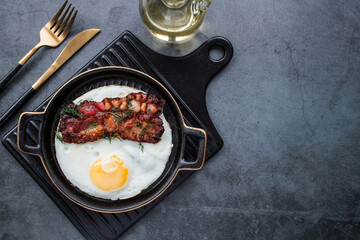 Fried eggs on a stylish ceramic plate with handles with fried bacon on a dark background. Breakfast, lunch and dinner. Delicious food. Cooking.