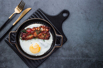 Fried eggs on a stylish ceramic plate with handles with fried bacon on a dark background. Breakfast, lunch and dinner. Delicious food. Cooking.
