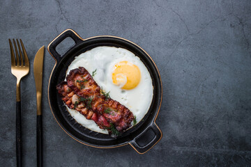 Fried eggs on a stylish ceramic plate with handles with fried bacon on a dark background. Breakfast, lunch and dinner. Delicious food. Cooking.