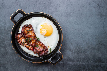 Fried eggs on a stylish ceramic plate with handles with fried bacon on a dark background. Breakfast, lunch and dinner. Delicious food. Cooking.