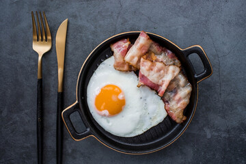 Fried eggs on a stylish ceramic plate with handles with fried bacon on a dark background. Breakfast, lunch and dinner. Delicious food. Cooking.