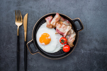 Fried eggs on a stylish ceramic plate with handles with fried bacon and cherry tomatoes on a dark background. Breakfast, lunch and dinner. Delicious food. Cooking.