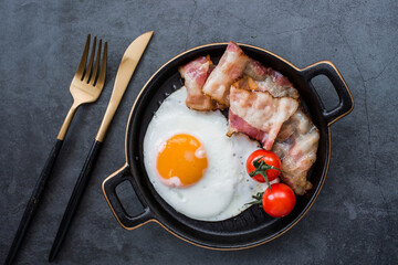 Fried eggs on a stylish ceramic plate with handles with fried bacon and cherry tomatoes on a dark background. Breakfast, lunch and dinner. Delicious food. Cooking.
