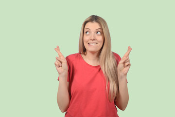 Young woman smiling while posing with fingers crossed for good luck isolated over green background