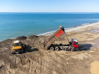 View from a drone on a bulldozer and a dump truck that dropped stones on the sea embankment on a...