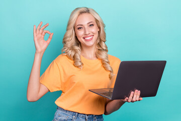 Photo of cute confident lady dressed orange t-shirt showing okey gesture texting modern gadget isolated teal color background