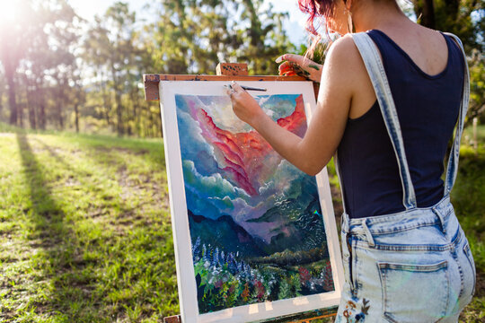 Young artist in overalls painting art outside in nature