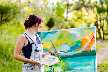 Young female artist with sketchbook reference book working on painting outdoors