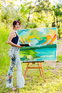 Young female artist with sketchbook reference book working on painting outdoors
