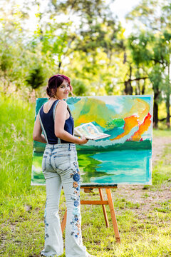 Young female artist with sketchbook reference book working on painting outdoors