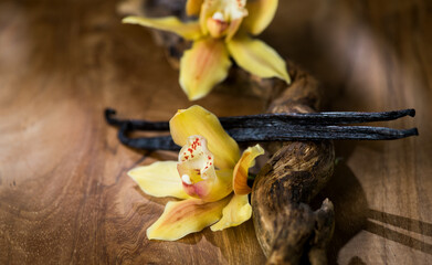 Vanilla flowers and pods close up. Vanilla beans over wooden background, macro shot. Aromatic condiments closeup, flavour