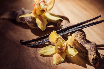 Vanilla flowers and pods close up. Vanilla beans over wooden background, macro shot. Aromatic condiments closeup, flavour
