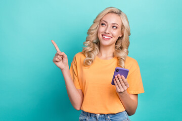 Portrait of optimistic person wear stylish t-shirt hold smartphone look indicating empty space isolated on turquoise color background