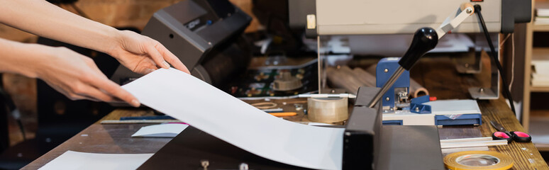 cropped view of woman holding paper next to paper trimmer in print center, banner.