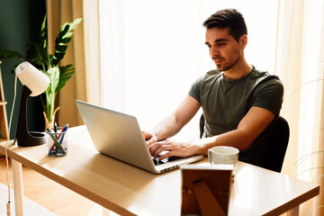 Young man sits at a desk at home and using laptop