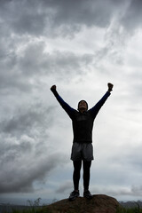 Triumph at the top. A young man celebrating at the top of a mountain after reaching the summit.