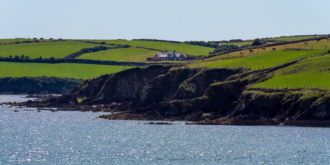 Fototapeta na wymiar A small house on a rocky Irish shore on a sunny summer day. Atlantic coast of Ireland, landscape. Green hills. Green grass field