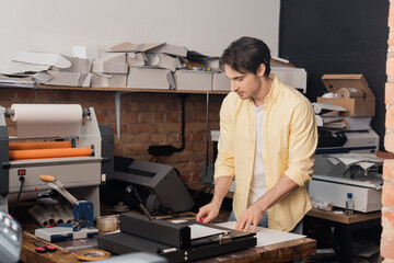 good looking typographer cutting paper with knife near paper trimmer in print center.