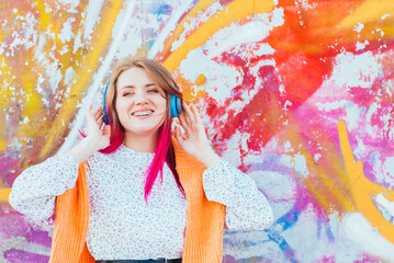 Portrait of a young laughing girl with braces listening to music in headphones in the summer on the street