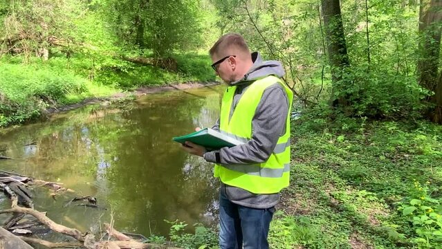 Male ecologist makes records of the state of the environment forest river. Environmental control.