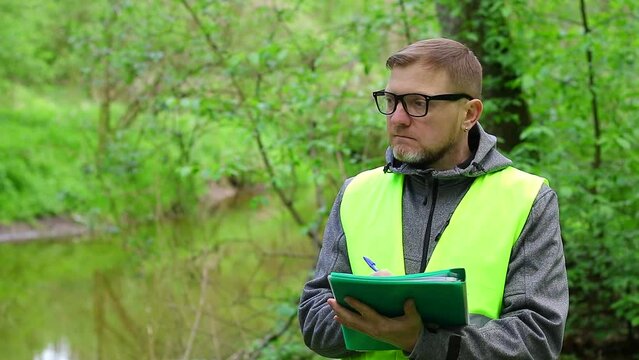 Male ecologist makes records of the state of the environment forest river. Environmental control.