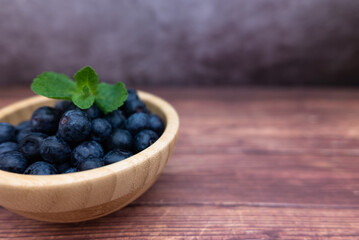 Fresh blueberries in a wooden bowl with some mint. Selective focus.