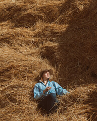 Naklejka na ściany i meble A woman in work clothes and a straw hat rests on a haystack