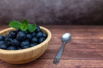 Fresh blueberries in a wooden bowl with some mint. Teaspoon, selective focus.