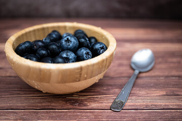 Freshly washed blueberries in a wooden bowl placed on a table. Selective focus, water drops.