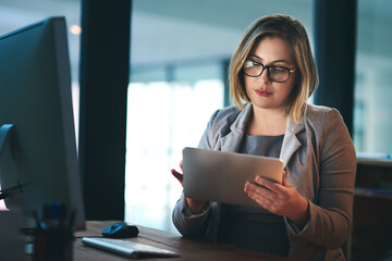 Using technology to brush up on some final touches. a young businesswoman working late on a digital tablet in an office.