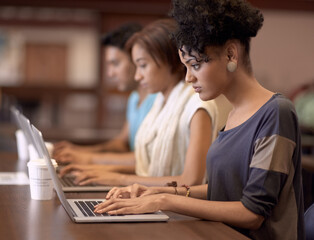 Studying diligently on her laptop. a young student working on her laptop with other students in the...