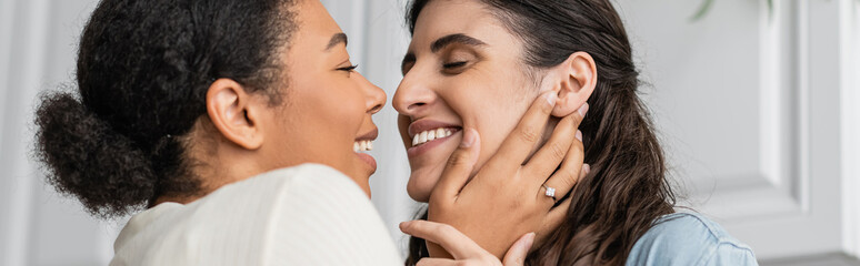 overjoyed multiracial woman with engagement ring on finger hugging girlfriend, banner.