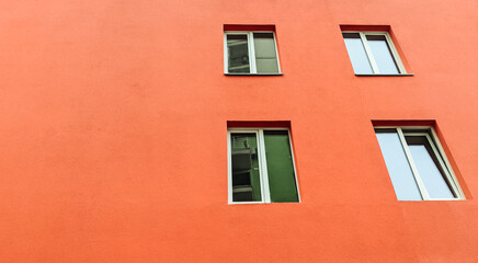 Fototapeta na wymiar Red wall exterior with four modern glass windows. Deep orange stucco wall paint.Copy space.