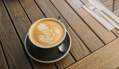 Business lunch espresso mug in woman hands. cappuccino in grey cup on the vintage wooden table. Floral latte art. 
