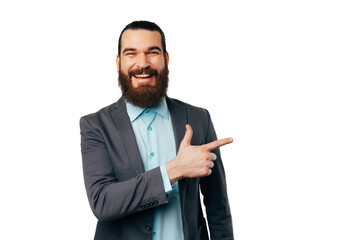 Handsome smiling bearded man wearing a jacket is pointing aside at white copy space.