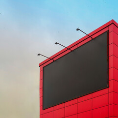 Empty black billboard with backlight on the wall of the building against the sky. Billboard mockup for advertising on the wall of the mall